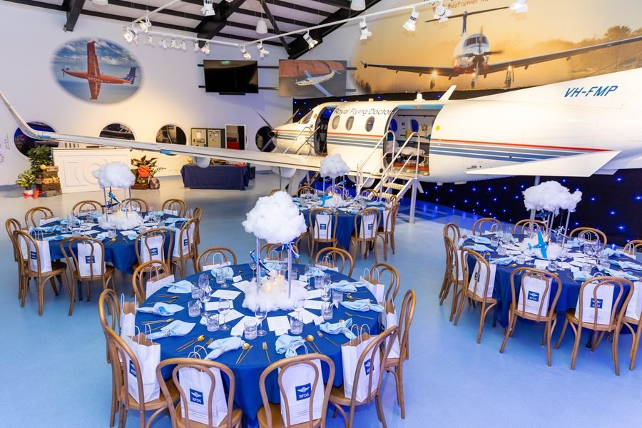 Hangar set for dinner with navy linen and cloud centrepieces beneath the aircraft