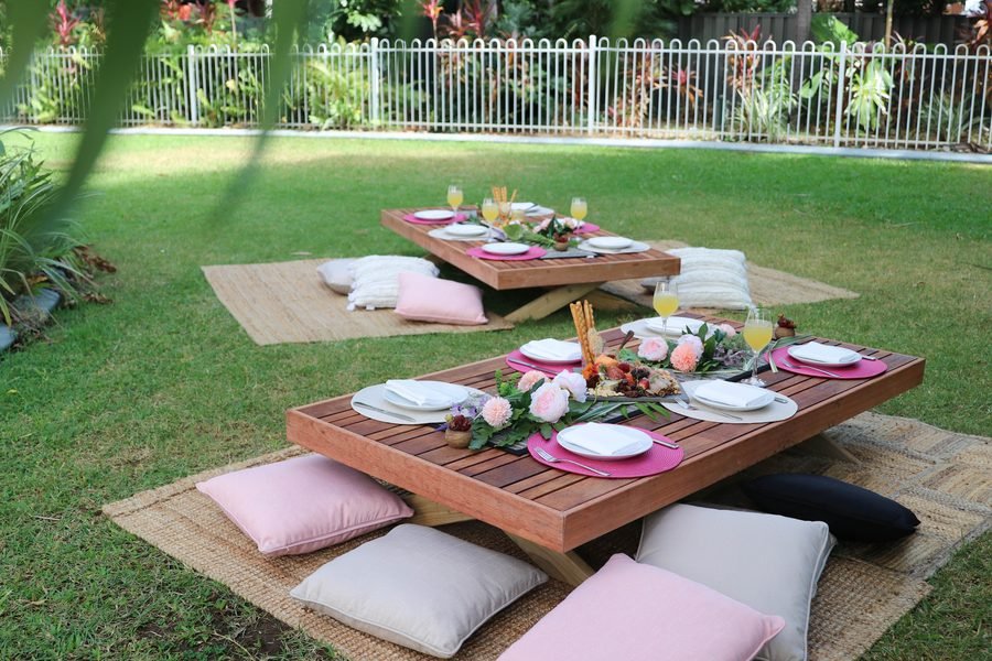 Low picnic table with pink cushions under palms on a lawn