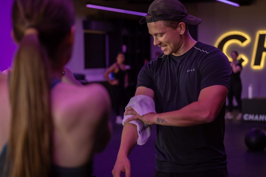 Coach talking a member through a set, towel over his arm, class running behind