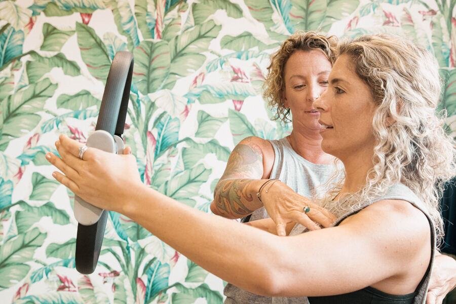 Instructor guiding a member holding a pilates ring, palm-print wall behind