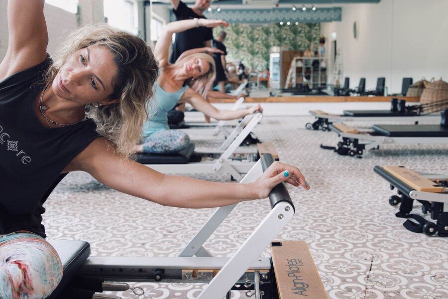 Instructor mid side-stretch on the reformer, looking to camera