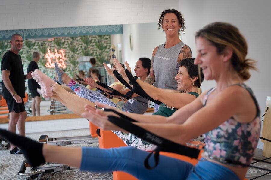 Row of members laughing with their legs in the reformer straps