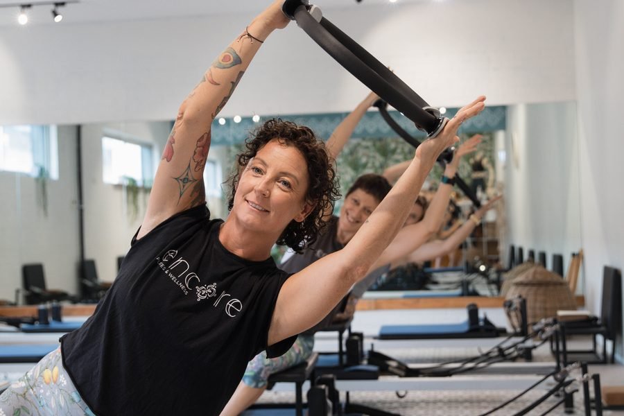 Instructor reaching overhead on the reformer, class following