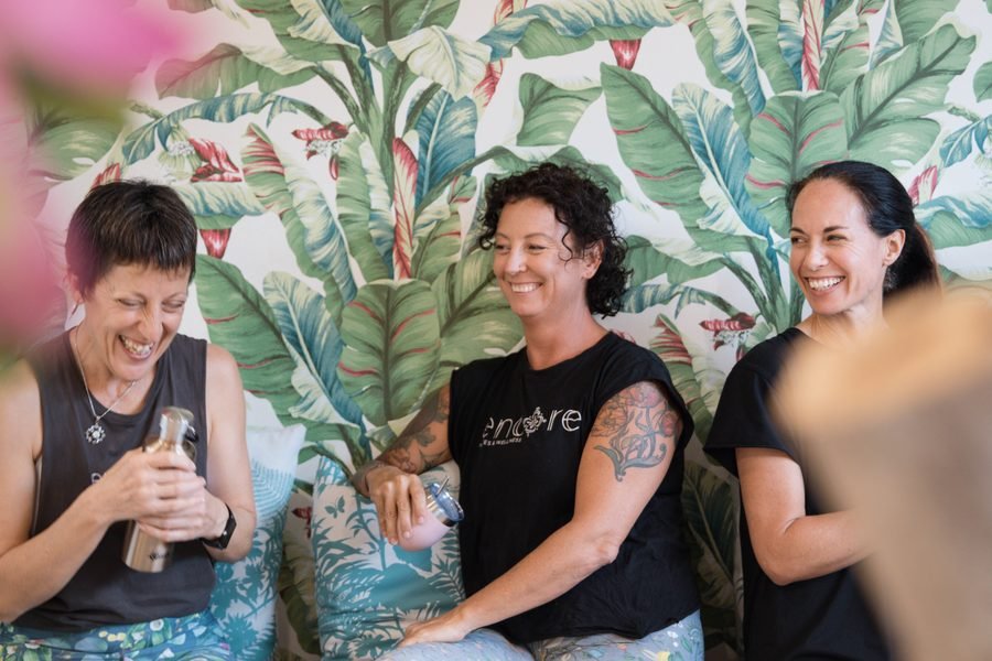 Three instructors laughing together against a palm print wall