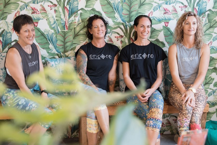 Four instructors in branded tees seated together, greenery in the foreground