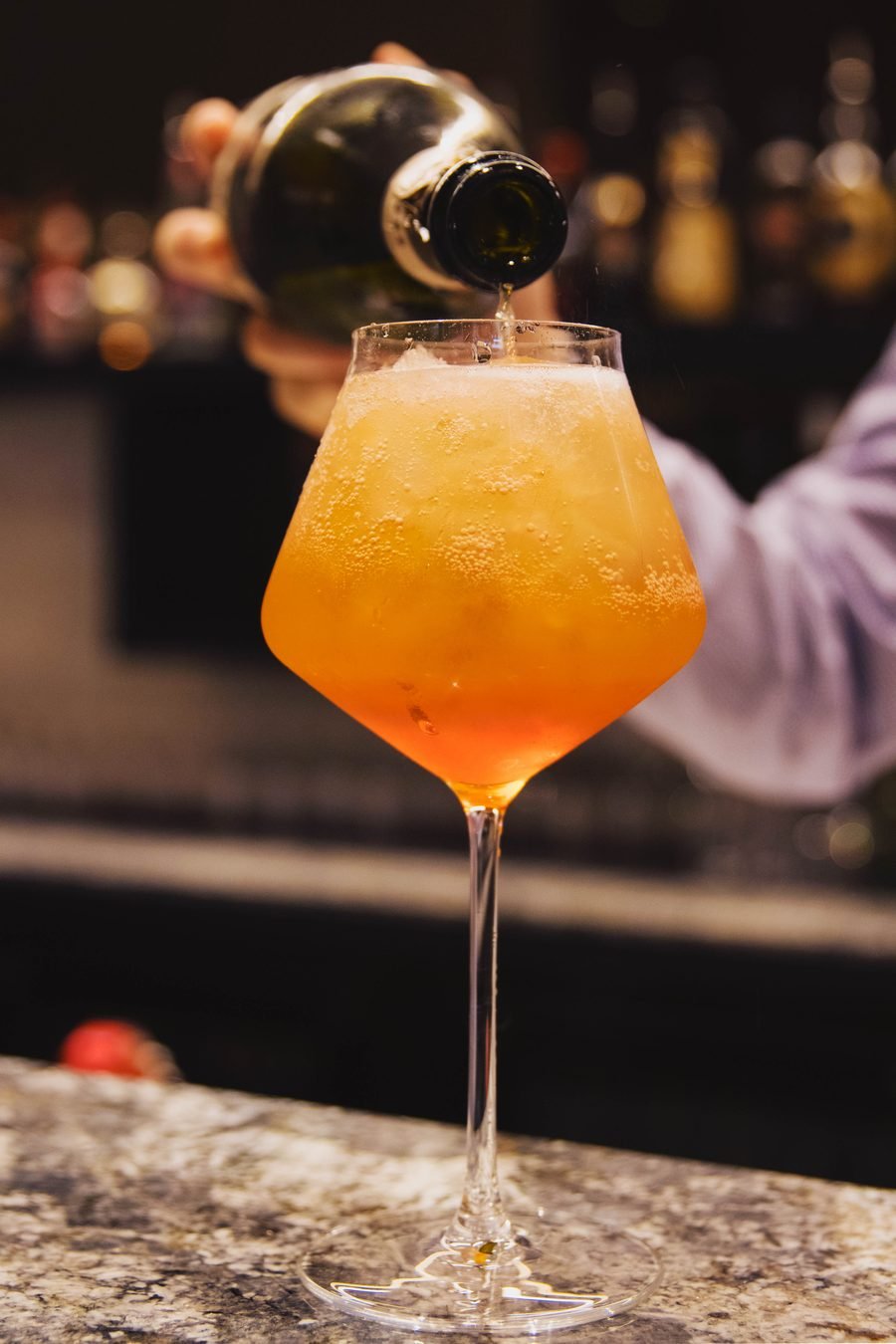 Guest holding a garnished orange cocktail to the light