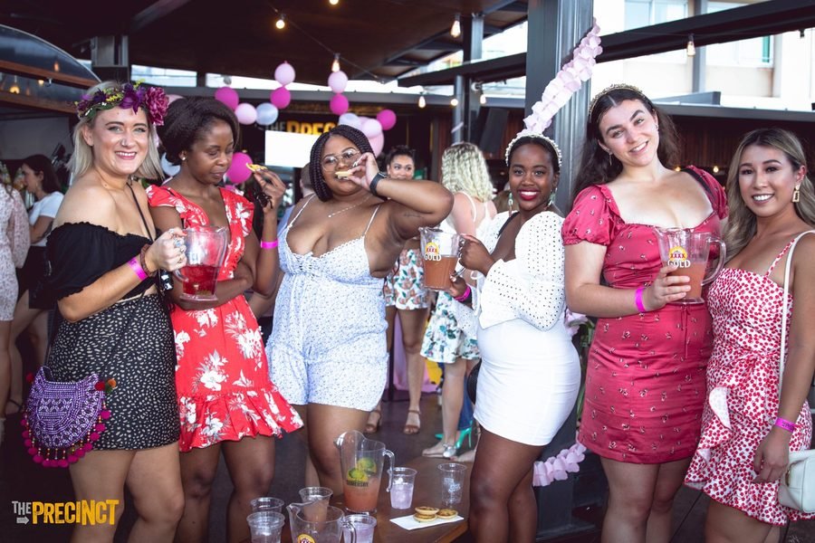 Group of guests in flower crowns raising drinks at the bar