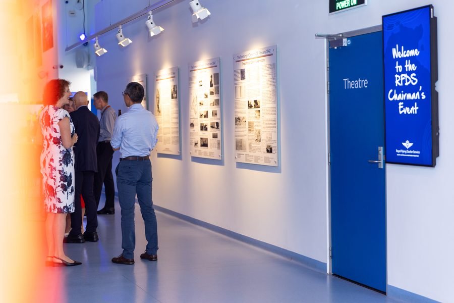 Guests moving along the exhibit wall in warm corridor light