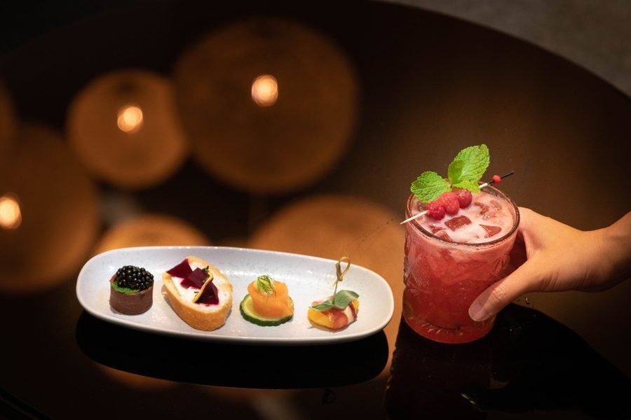 Canapes and a berry cocktail with bar lights blurred behind