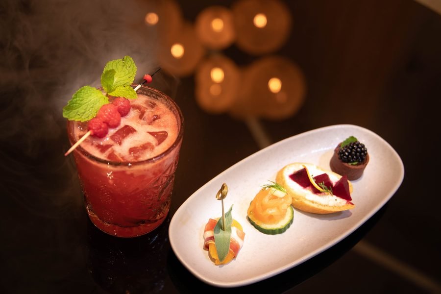 Berry cocktail with mint beside a plate of canapes