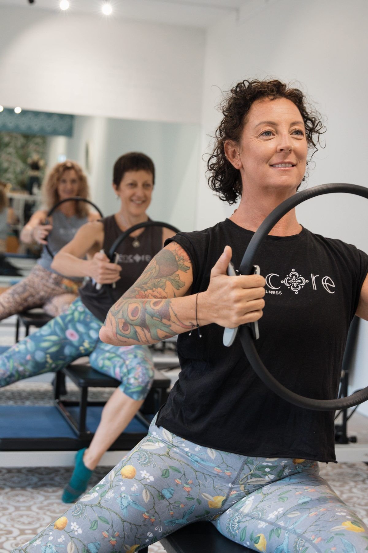 Instructor kneeling with a pilates ring, smiling, studio behind