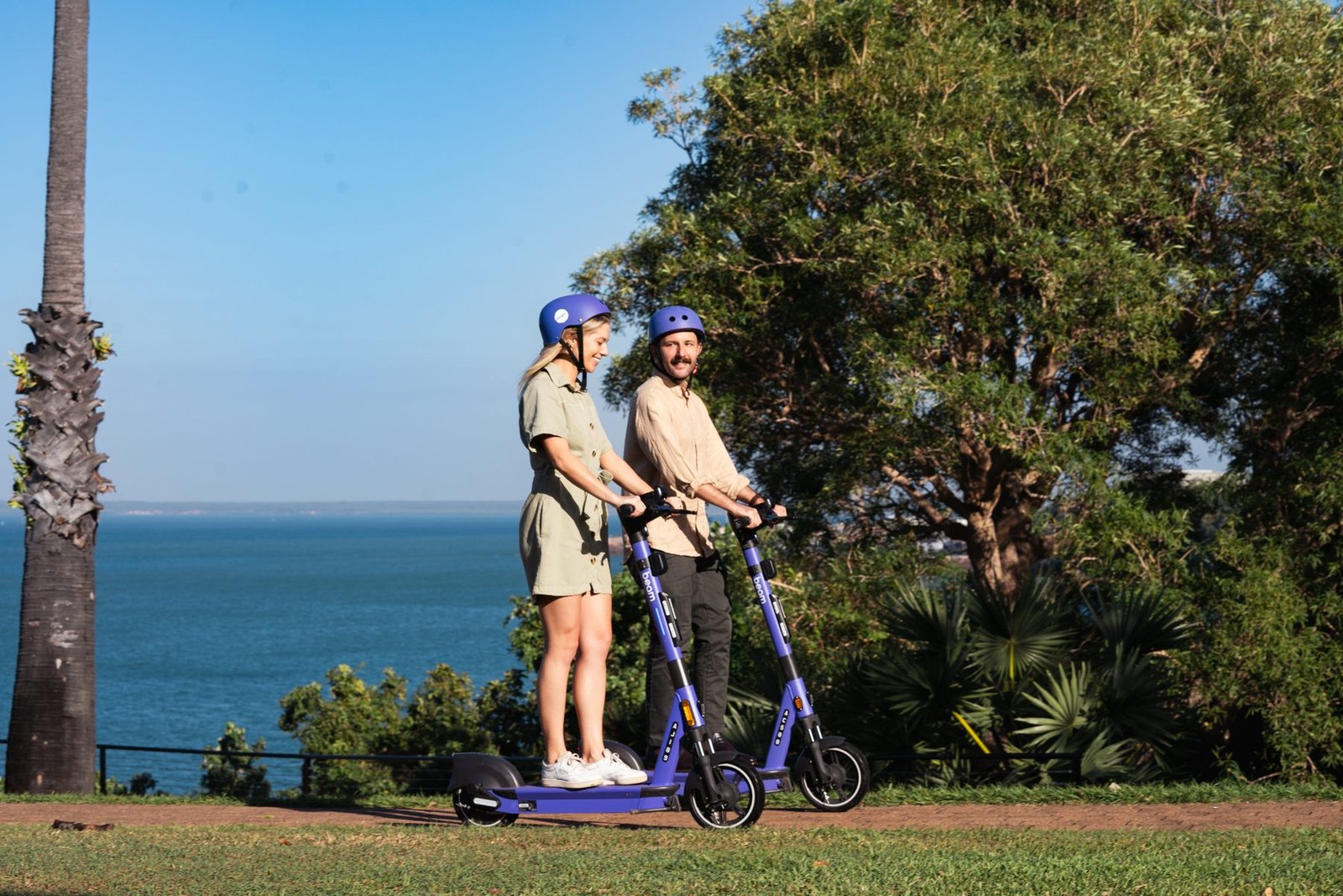Two riders on Beam scooters pausing on the headland above the sea