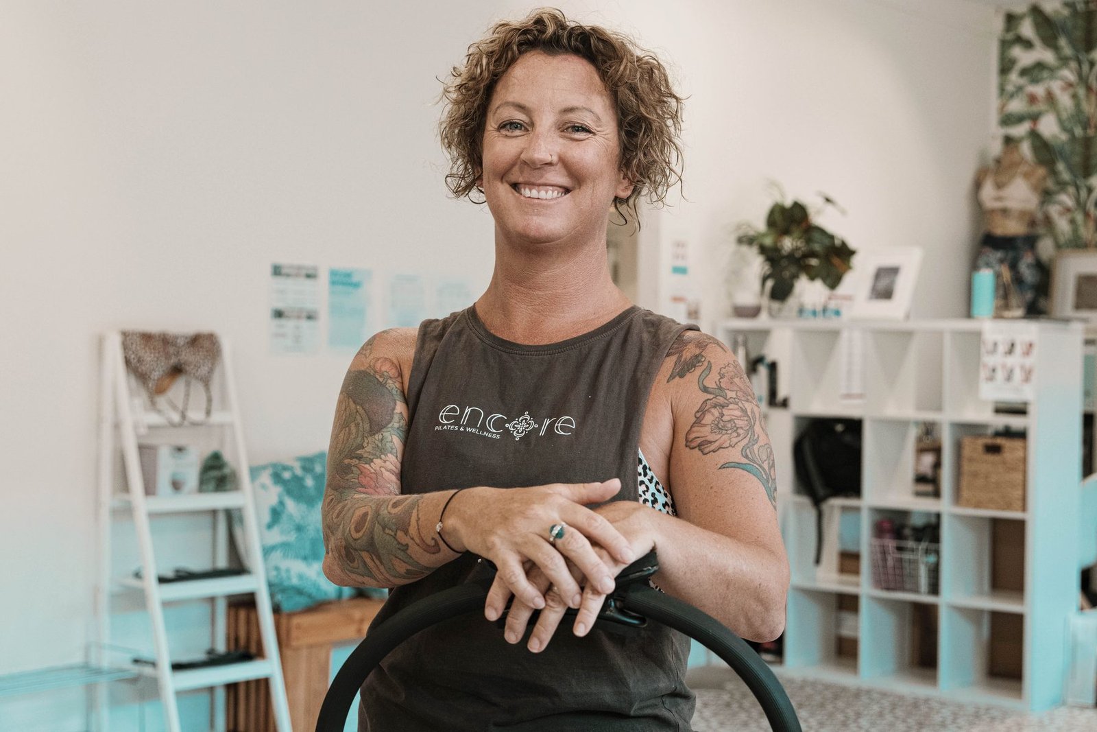 Instructor seated with a pilates ring, studio shelving behind