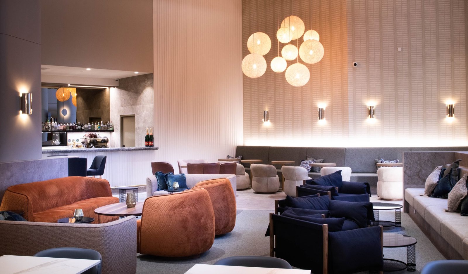 Hotel lounge with woven pendant lights, tan armchairs and the bar beyond